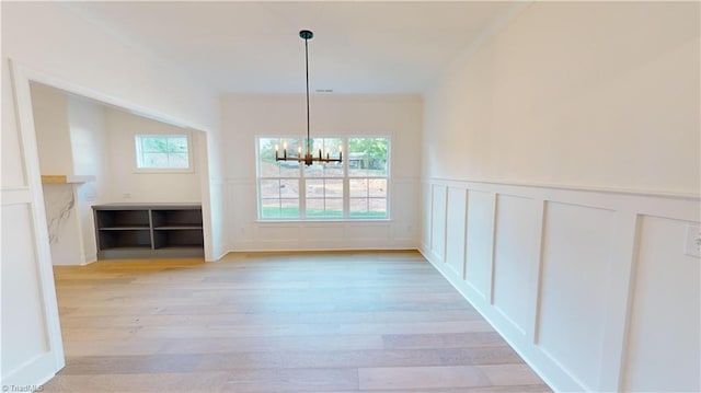 unfurnished dining area featuring light wood-style floors, wainscoting, a decorative wall, and an inviting chandelier