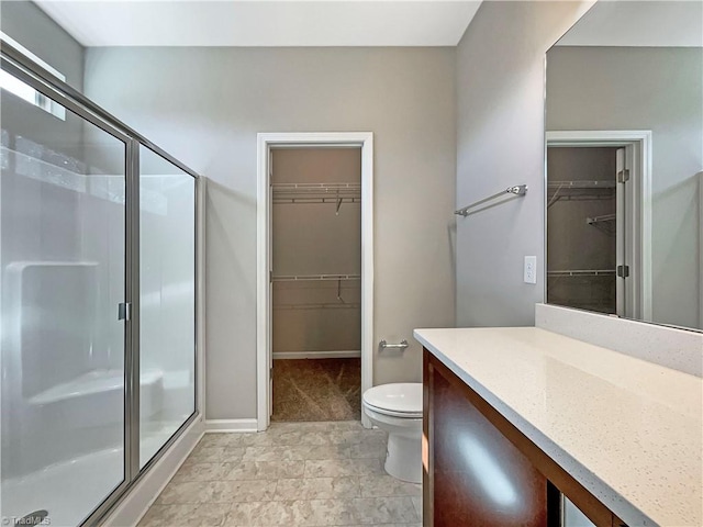 bathroom featuring toilet, vanity, baseboards, a spacious closet, and a shower stall