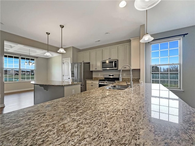 kitchen with stone countertops, coffered ceiling, a kitchen island, a sink, and appliances with stainless steel finishes