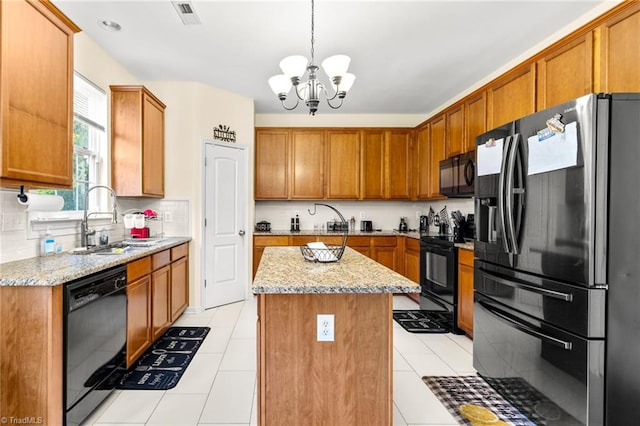 kitchen with light stone counters, hanging light fixtures, black appliances, sink, and a kitchen island