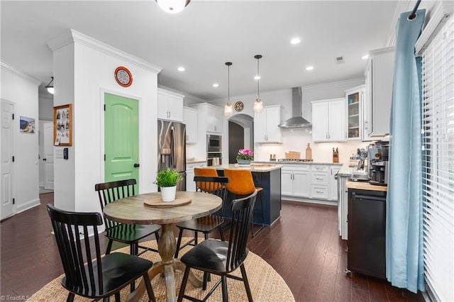 kitchen featuring a center island, wall chimney range hood, light countertops, appliances with stainless steel finishes, and arched walkways