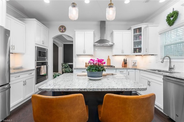 kitchen featuring a kitchen island, arched walkways, stainless steel appliances, wall chimney exhaust hood, and a sink