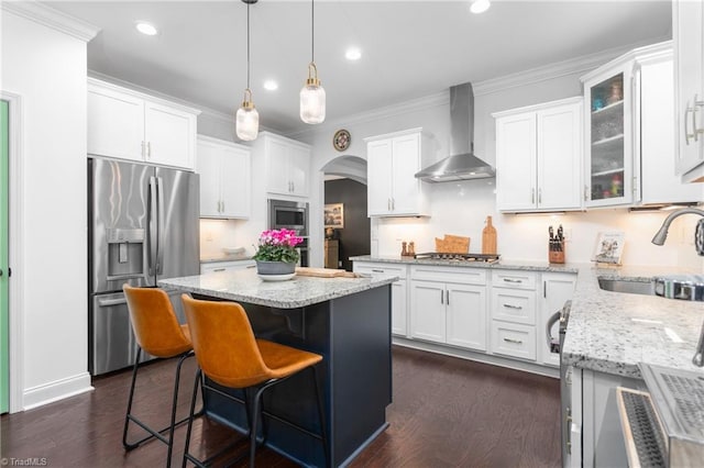 kitchen with a sink, white cabinetry, arched walkways, appliances with stainless steel finishes, and wall chimney range hood