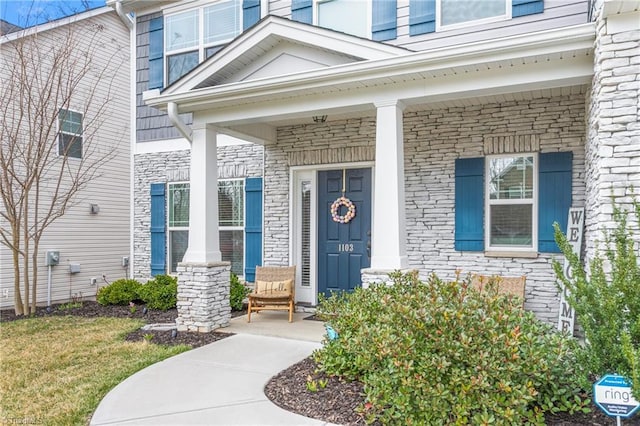 view of exterior entry with stone siding and covered porch