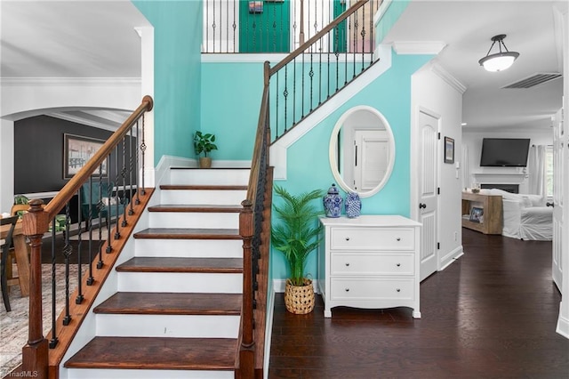 stairs with visible vents, ornamental molding, a fireplace, wood finished floors, and arched walkways