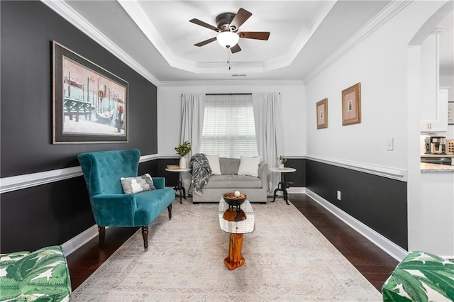 sitting room featuring a raised ceiling, arched walkways, wood finished floors, and crown molding