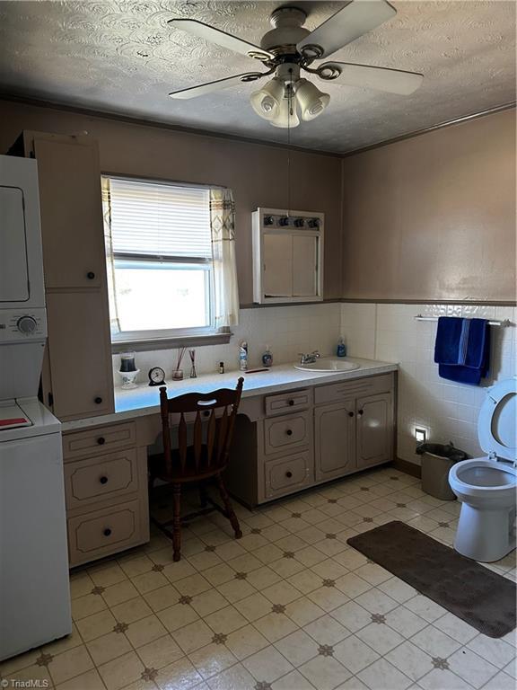 bathroom featuring stacked washer / drying machine, wainscoting, a textured ceiling, and tile patterned floors