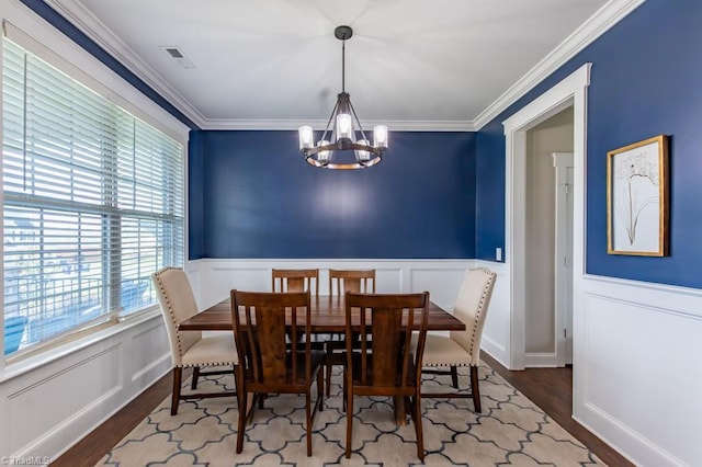 dining space with a notable chandelier, visible vents, ornamental molding, wainscoting, and wood finished floors