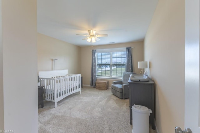 bedroom featuring a crib, ceiling fan, baseboards, and carpet flooring