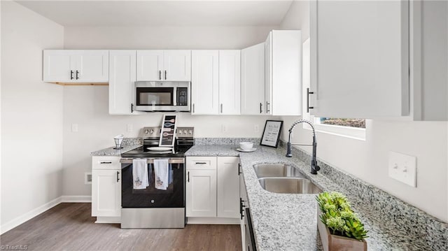 kitchen with hardwood / wood-style floors, sink, appliances with stainless steel finishes, light stone counters, and white cabinetry