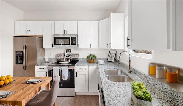 kitchen featuring white cabinets, sink, light hardwood / wood-style flooring, light stone countertops, and stainless steel appliances