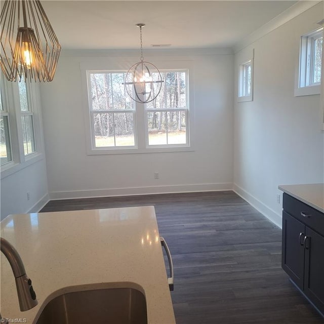 unfurnished dining area with a sink, an inviting chandelier, crown molding, baseboards, and dark wood-style flooring