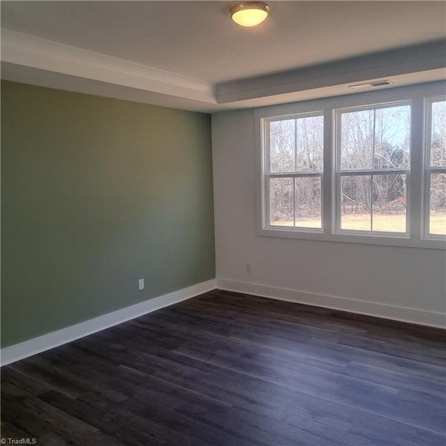 empty room featuring visible vents, a tray ceiling, baseboards, and dark wood-style flooring