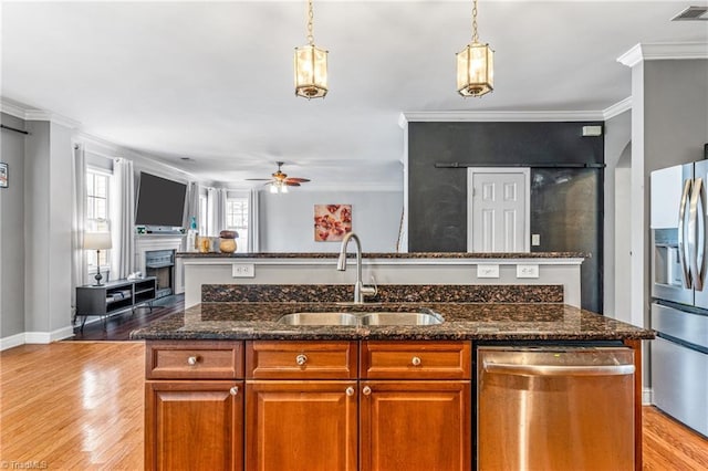 kitchen featuring sink, appliances with stainless steel finishes, ornamental molding, a center island with sink, and dark stone counters