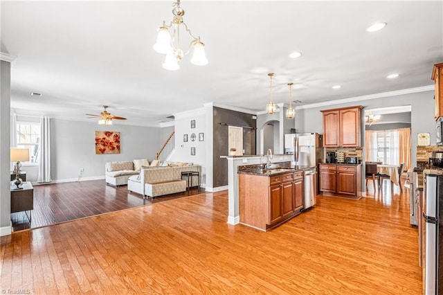 kitchen with sink, appliances with stainless steel finishes, a kitchen island with sink, hanging light fixtures, and light wood-type flooring