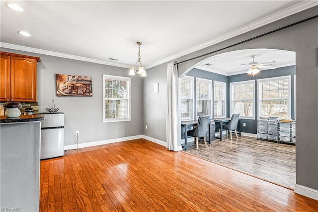 unfurnished dining area featuring crown molding, ceiling fan with notable chandelier, and light hardwood / wood-style floors