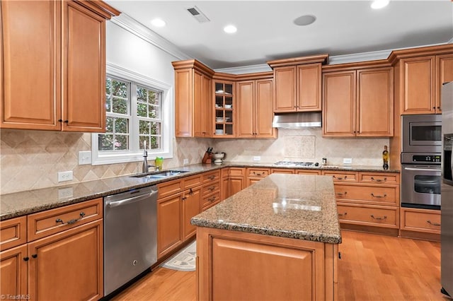 kitchen with sink, ornamental molding, appliances with stainless steel finishes, a kitchen island, and light stone countertops