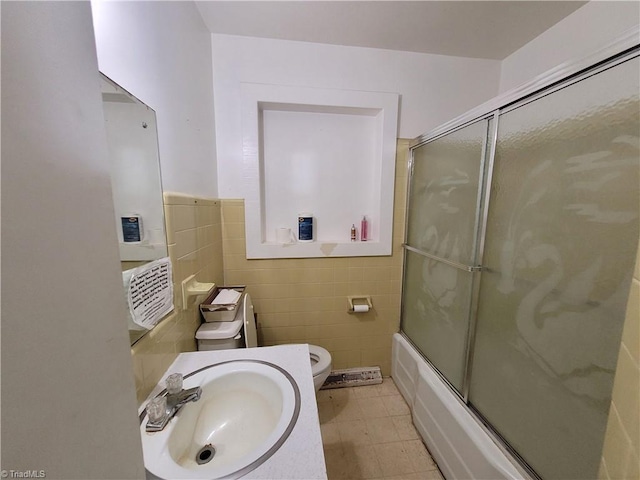 full bathroom with sink, combined bath / shower with glass door, tile walls, and toilet