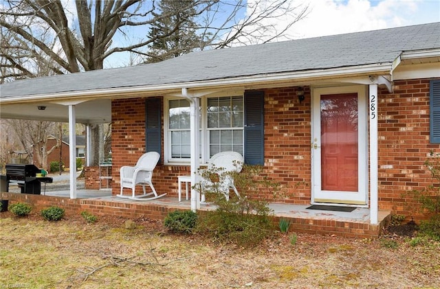 property entrance with covered porch, brick siding, roof with shingles, and an attached carport