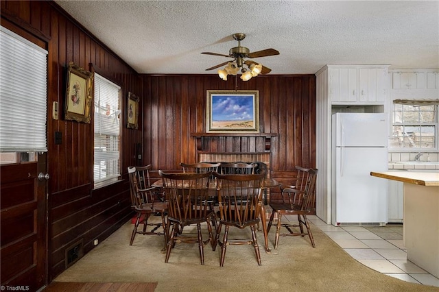 dining area featuring a textured ceiling, a healthy amount of sunlight, light tile patterned floors, and wooden walls