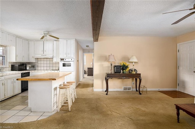 kitchen with oven, under cabinet range hood, white cabinets, and light colored carpet