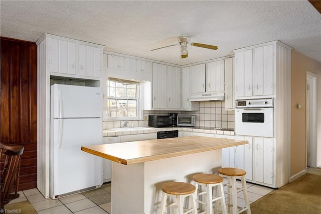 kitchen with white appliances, decorative backsplash, a textured ceiling, under cabinet range hood, and light tile patterned flooring