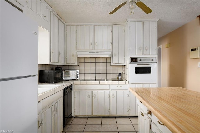 kitchen featuring light tile patterned flooring, under cabinet range hood, black appliances, and tile countertops