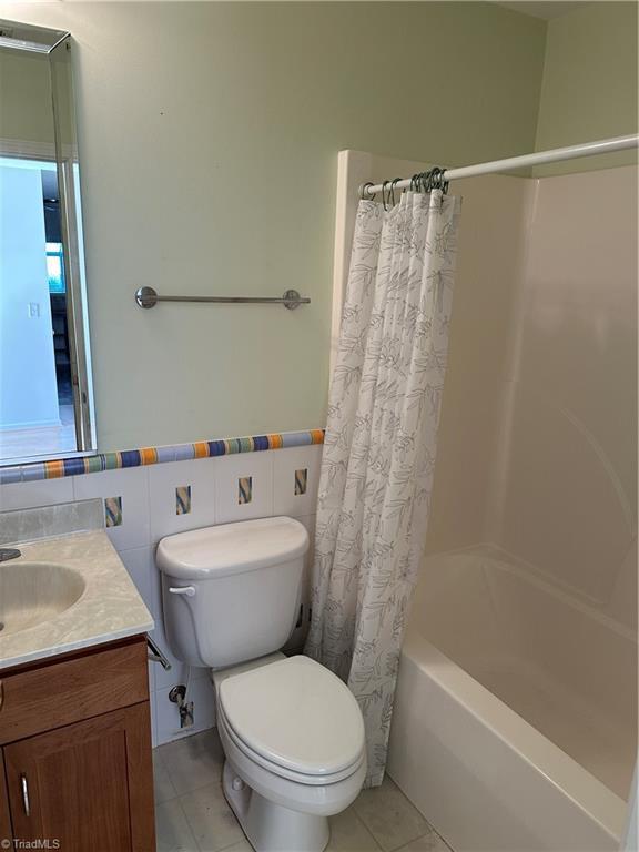 135 Plantation Place Ln, Mount Airy, NC 27030 - bathroom featuring vanity, shower / bathtub combination with curtain, tile patterned floors, tile walls, and a wainscoted wall