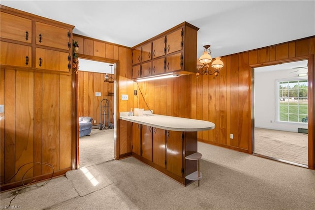 520 S Bunker Hill Rd, Colfax, NC 27235 - kitchen with light colored carpet, wood walls, brown cabinets, a chandelier, and a peninsula