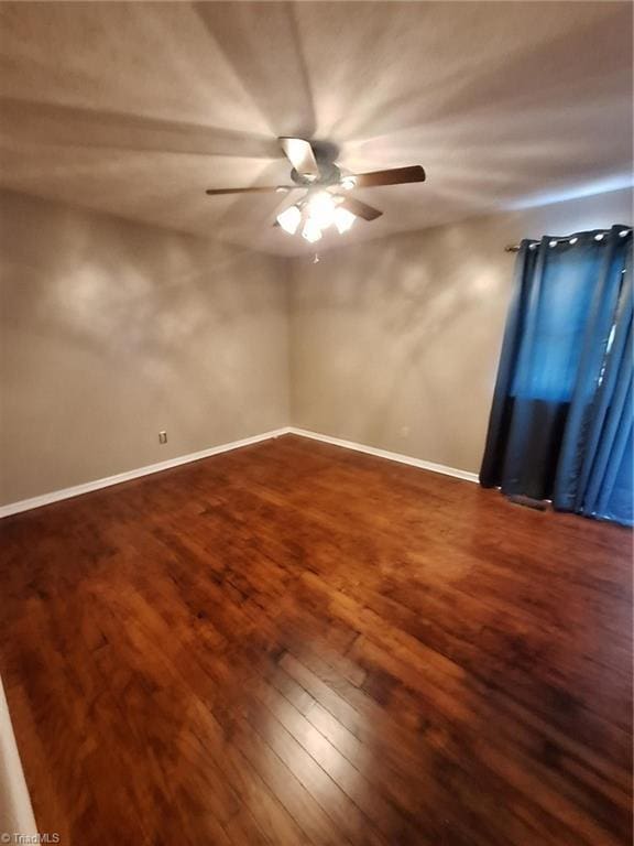 empty room featuring ceiling fan, dark wood finished floors, and baseboards