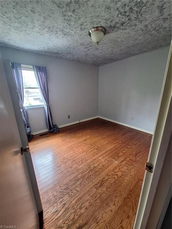 empty room featuring wood finished floors, baseboards, and a textured ceiling
