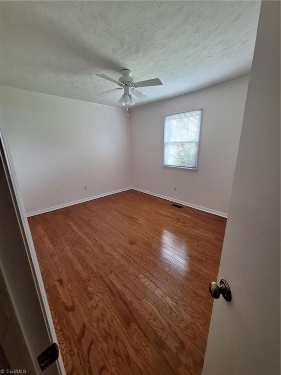 unfurnished room featuring a ceiling fan, wood finished floors, baseboards, and a textured ceiling