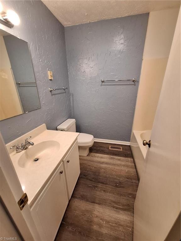 full bathroom with wood finished floors, toilet, a textured wall, vanity, and baseboards