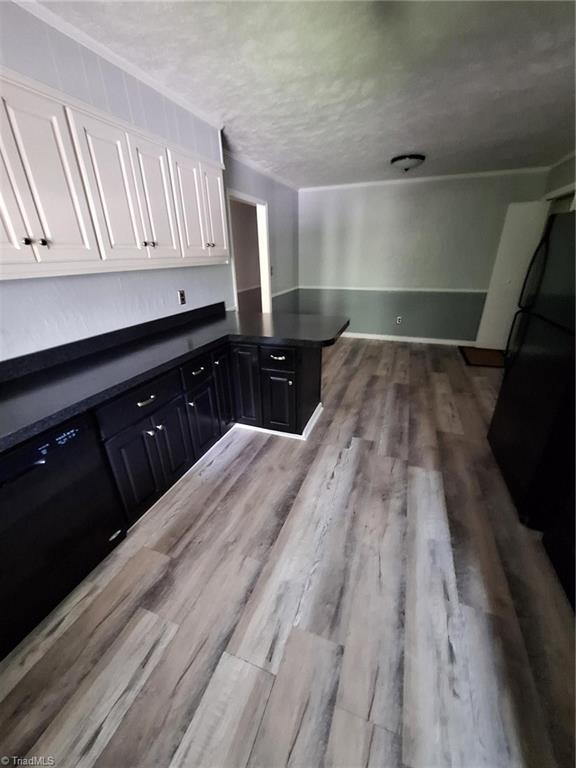 kitchen with dark countertops, white cabinetry, wood finished floors, freestanding refrigerator, and a textured ceiling