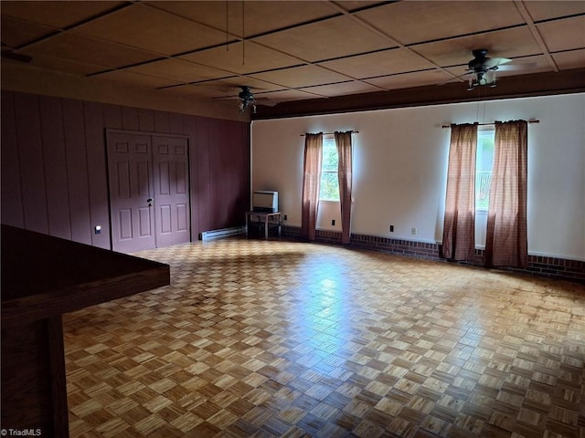 spare room featuring a ceiling fan, baseboards, baseboard heating, a drop ceiling, and wooden walls