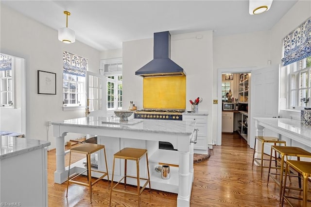 kitchen with a wealth of natural light, light stone countertops, hardwood / wood-style floors, and wall chimney exhaust hood