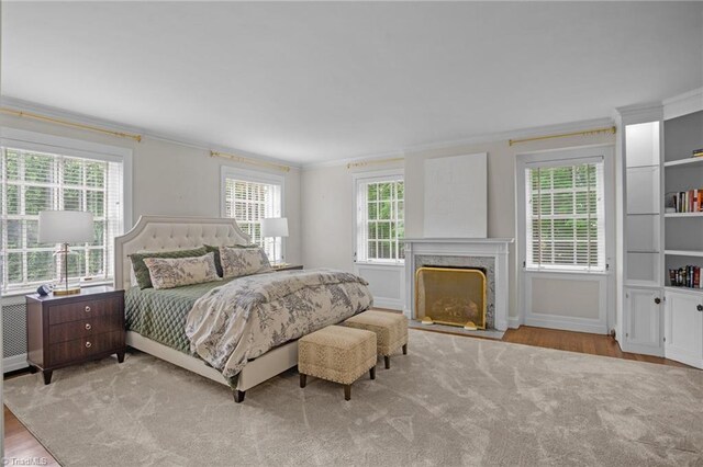 bedroom with ornamental molding, wood-type flooring, and a high end fireplace