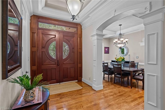 foyer featuring a notable chandelier, ornamental molding, decorative columns, and light wood-type flooring