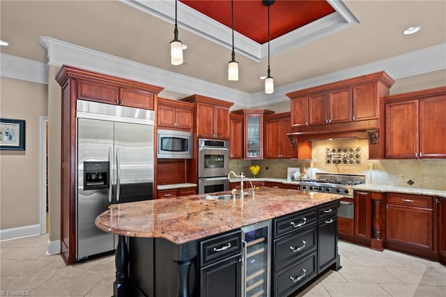 kitchen with pendant lighting, beverage cooler, a kitchen island with sink, built in appliances, and a raised ceiling