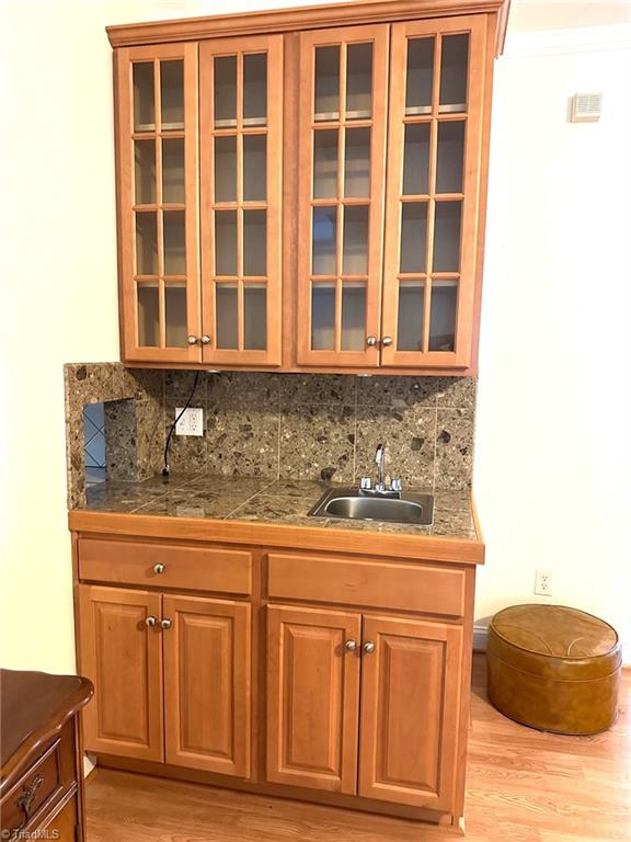 bar featuring a sink, tasteful backsplash, light wood-style floors, and wet bar