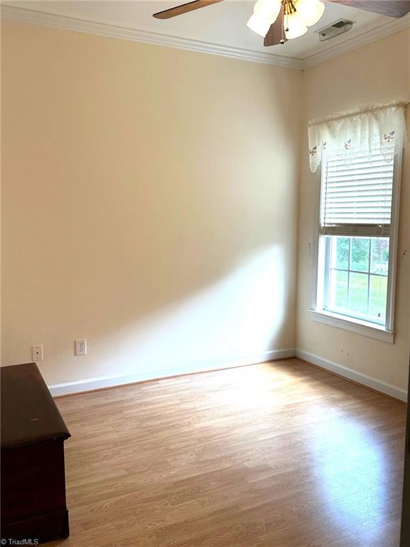 spare room with crown molding, visible vents, wood finished floors, baseboards, and ceiling fan