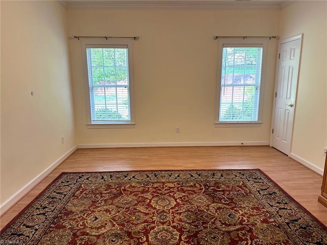 empty room featuring light wood-style floors, baseboards, and crown molding