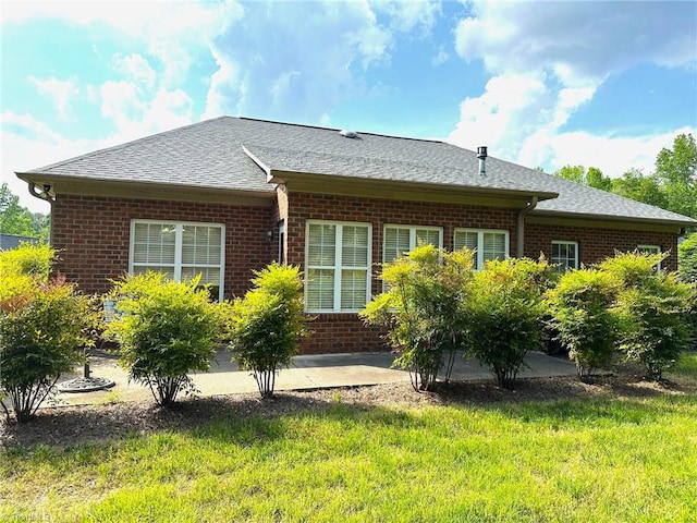 rear view of property with a lawn, a patio, a shingled roof, and brick siding