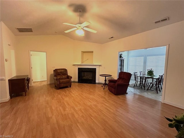 living room with wood finished floors, a ceiling fan, a tile fireplace, and visible vents