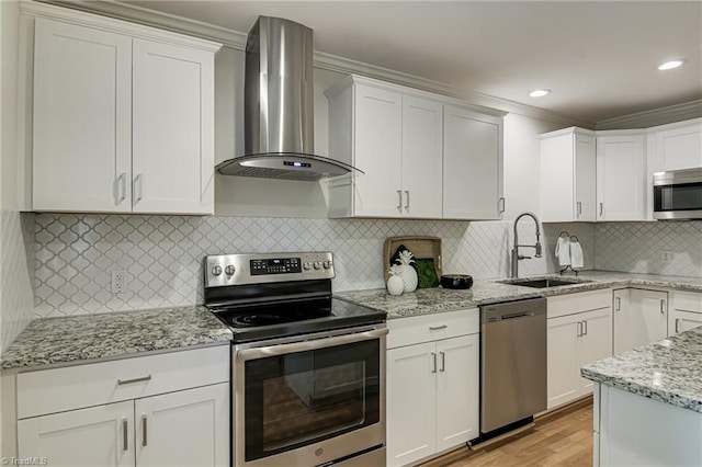 kitchen with stainless steel appliances, wall chimney exhaust hood, a sink, ornamental molding, and white cabinetry