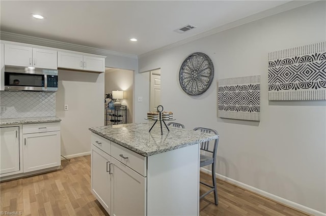 kitchen with stainless steel microwave, a breakfast bar area, light wood-style flooring, ornamental molding, and light stone countertops