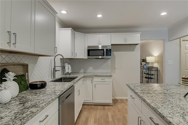 kitchen with appliances with stainless steel finishes, a sink, crown molding, light wood-style floors, and tasteful backsplash