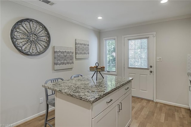 kitchen with a kitchen bar, light wood-style flooring, light stone counters, baseboards, and crown molding