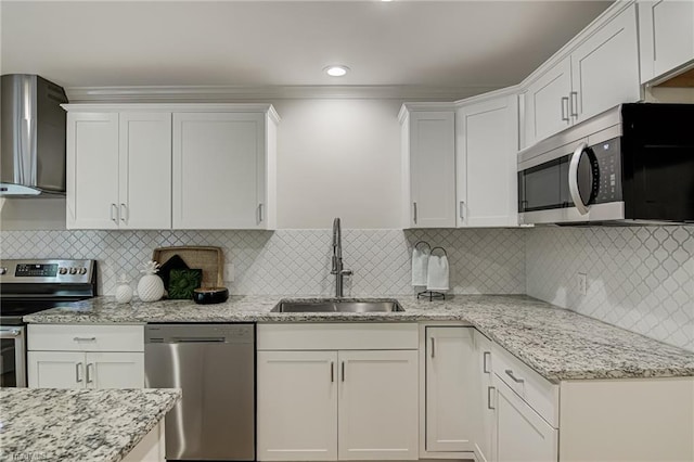 kitchen featuring appliances with stainless steel finishes, a sink, wall chimney exhaust hood, white cabinets, and light stone countertops