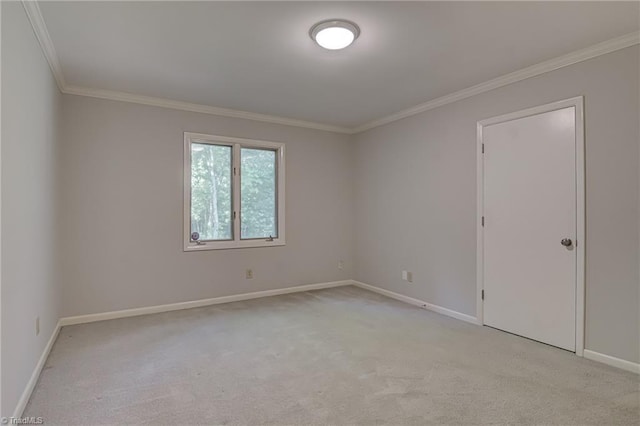 spare room featuring light carpet, crown molding, and baseboards